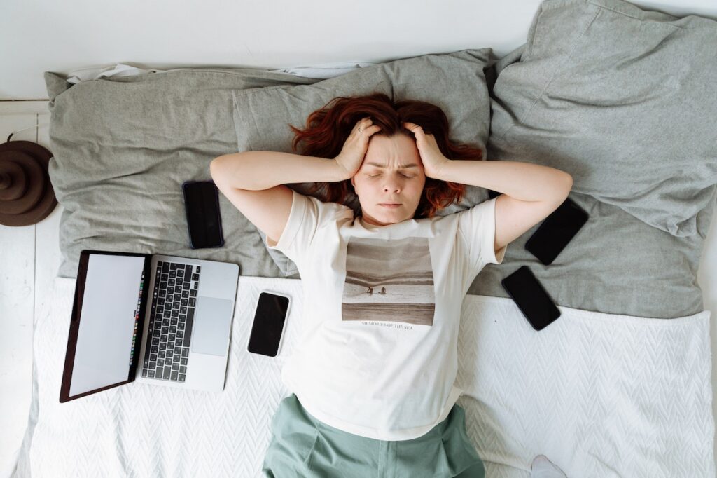 Woman stressed, surrounded by digital devices. 